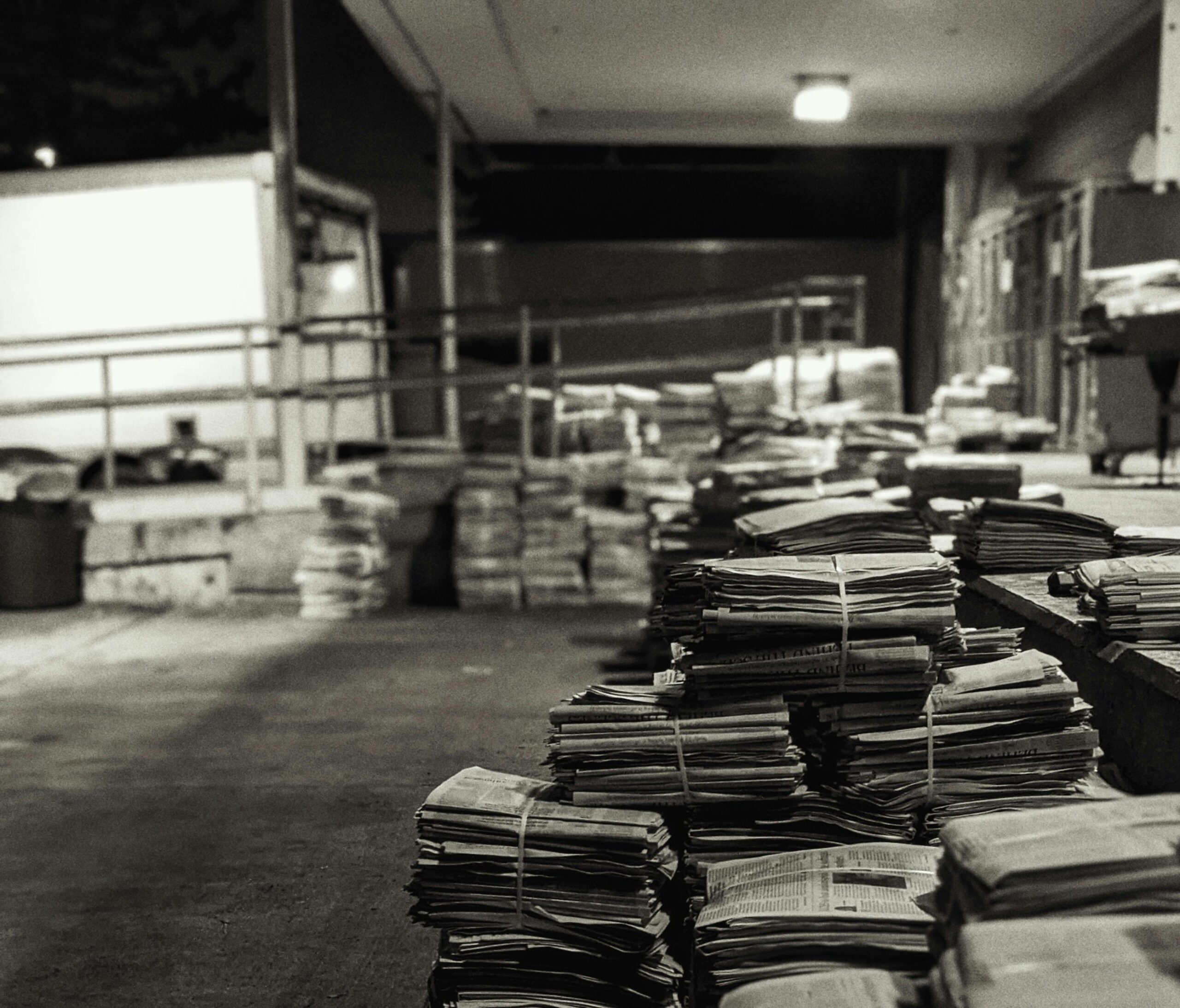 Stacks of newspapers in a warehouse, captured in black and white, creating a vintage feel.