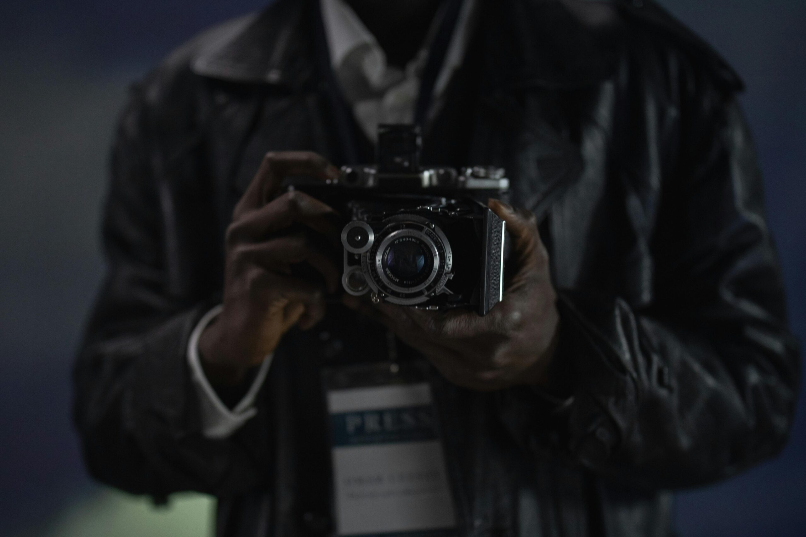 A close-up photograph of a person holding a vintage camera, possibly a reporter.